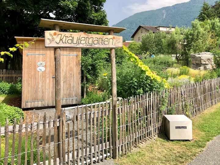 Ein Lattenzaun umgibt den Kräutergarten, über dem Eingang ist ein Schild.