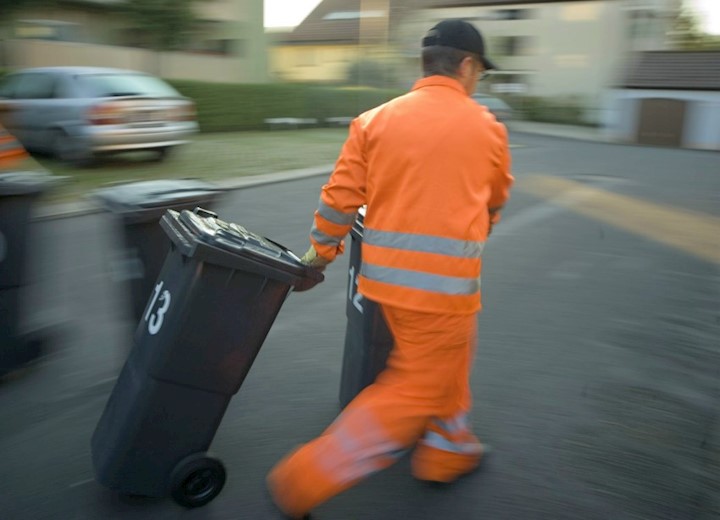 Ein Müllmann mit zwei schwarzen Abfallcontainern.